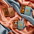 Two sets of Fragrance Wardrobe Deluxe perfume bottles in decorative boxes on a fabric background