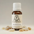 Bottle of Puja Perfumery Frankincense essential oil with frankincense resin on a neutral background