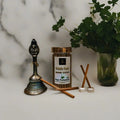 Pooja Perumary Fresh Feel Dhoop Sticks with a decorative bell and plant on a marble surface.