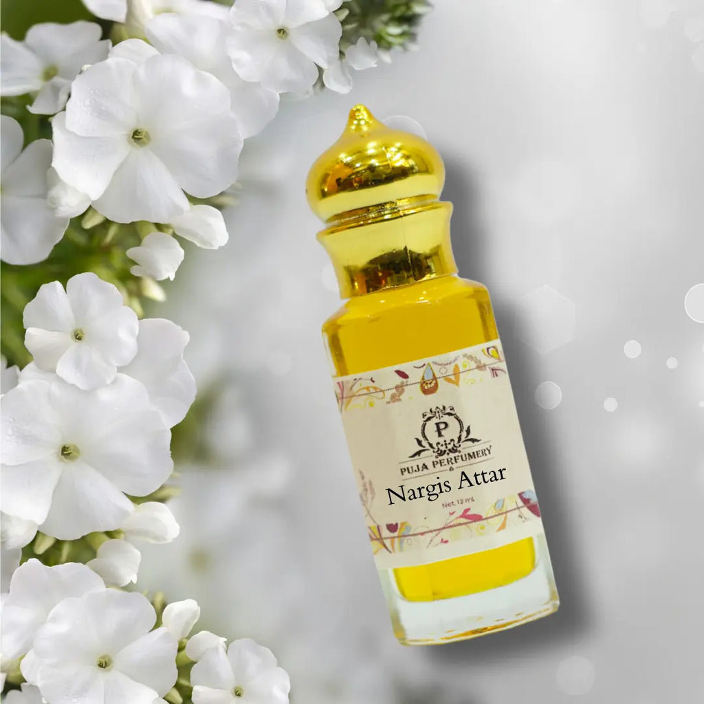 Bottle of Nargis Attar with a gold cap surrounded by white flowers on a light gray background