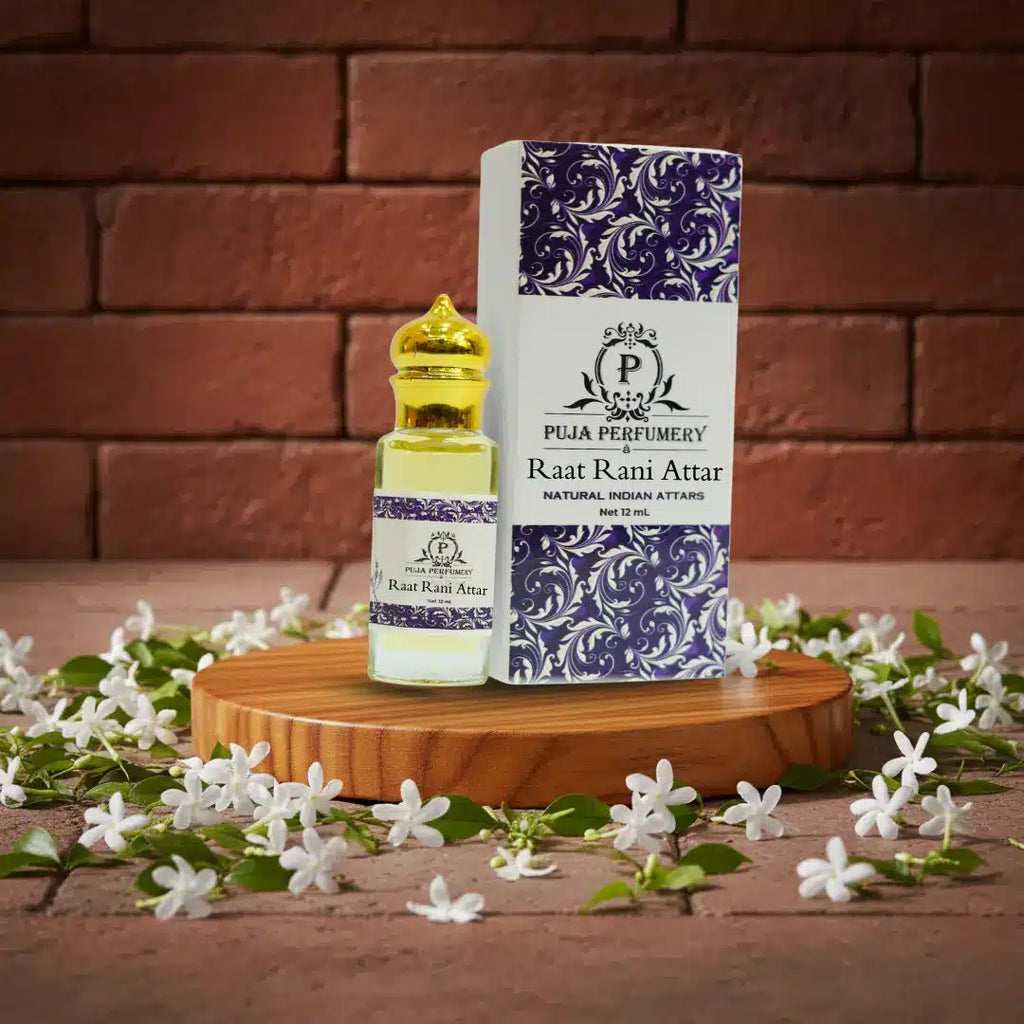 Puja Perfumery Raat Rani Attar bottle and packaging on a wooden stand with flowers and brick background