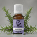 Bottle of Puja Perfumery Rosemary essential oil with rosemary sprigs on a gray background