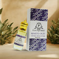 Puja Perfumery White Oud perfume bottle and packaging on a beige background with plants.
