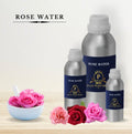 Bottles of rose water with a bowl of pink roses on a light background